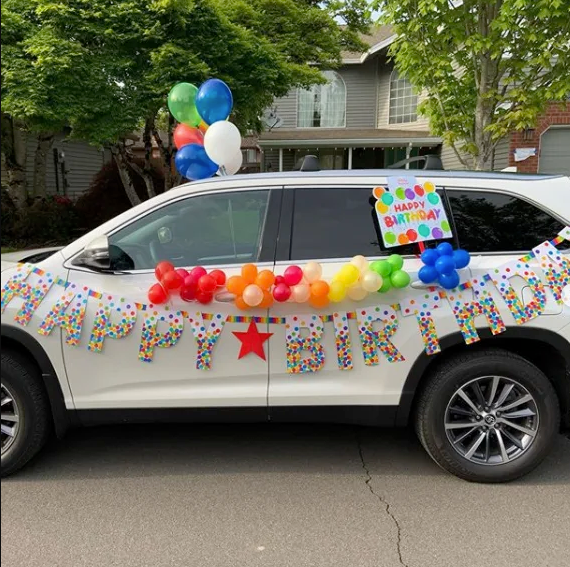 White car adorned with happy birthday sign and balloons
