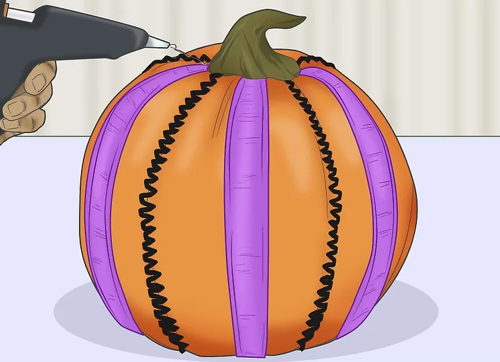 Hand holding glue gun gluing items on a pumpkin