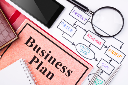 A paper with the words Business Plan written on it as well as another paper with a diagram and magnifying glass on top of it